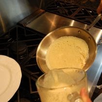 pouring crepe batter into frying pan on stove