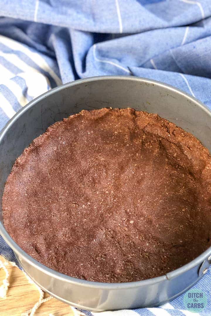 The chocolate almond flour crust is pressed into a metal cheesecake pan.