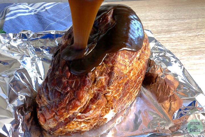 Pouring the glaze over the keto ham that is resting in a baking pan covered in foil.