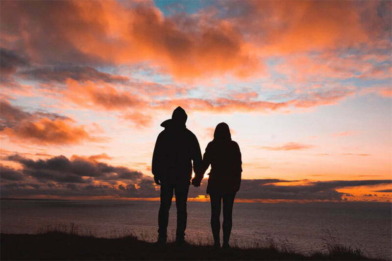 Silhouette of a couple holding hands, looking at sunset