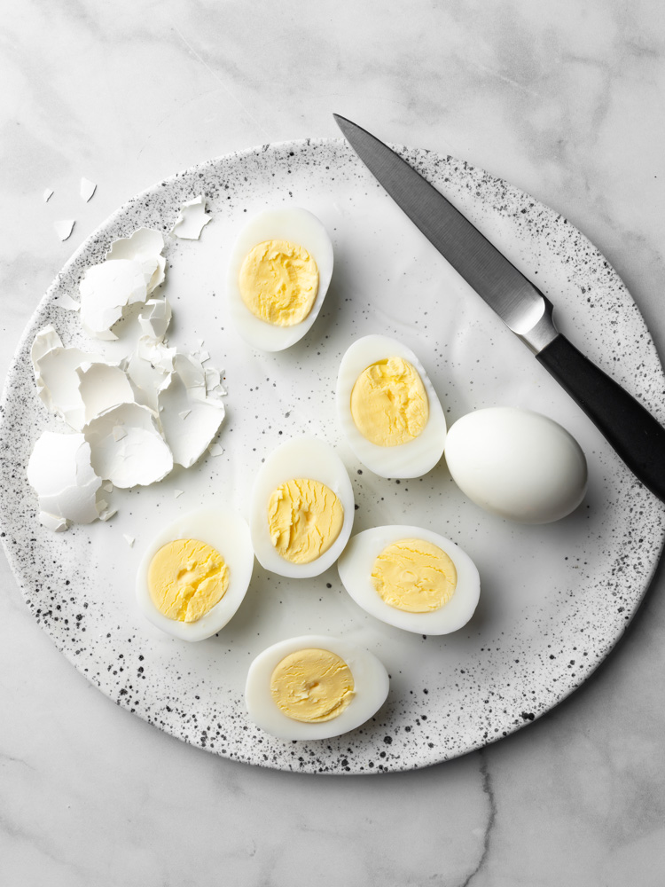 peeled boiled eggs on a plate with pieces of eggs sliced through showing the yolk