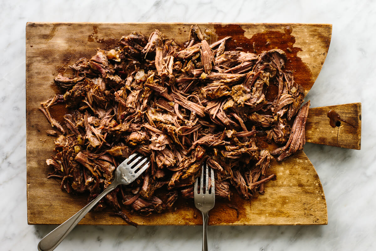 Shredded beef barbacoa on a wooden board with forks.