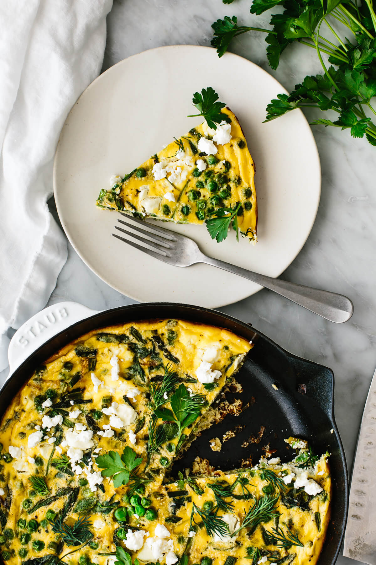 A skillet of spring vegetable frittata next to a plate with a fork.