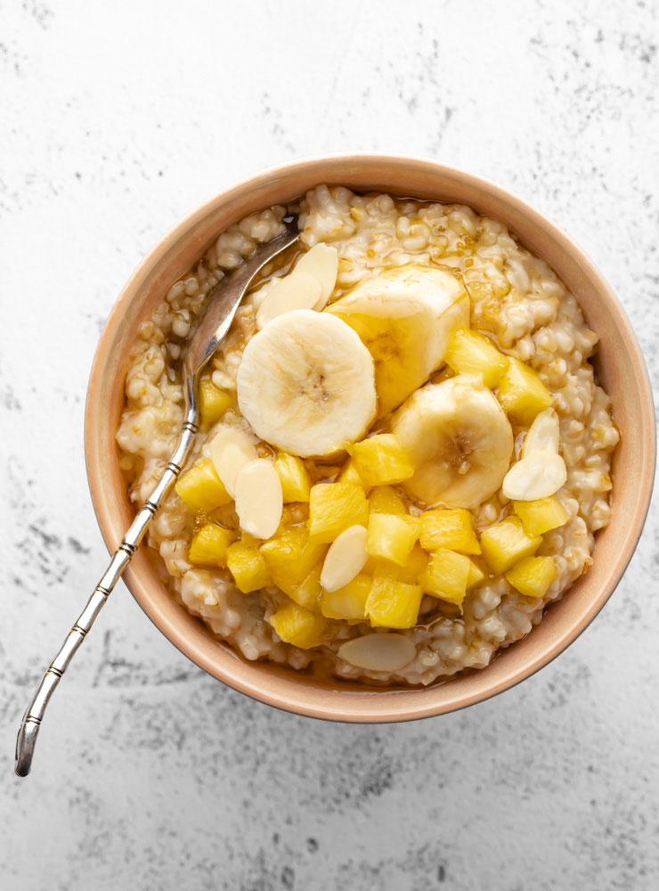 cooked oatmeal in a bowl topped with some pineapple, banana and honey
