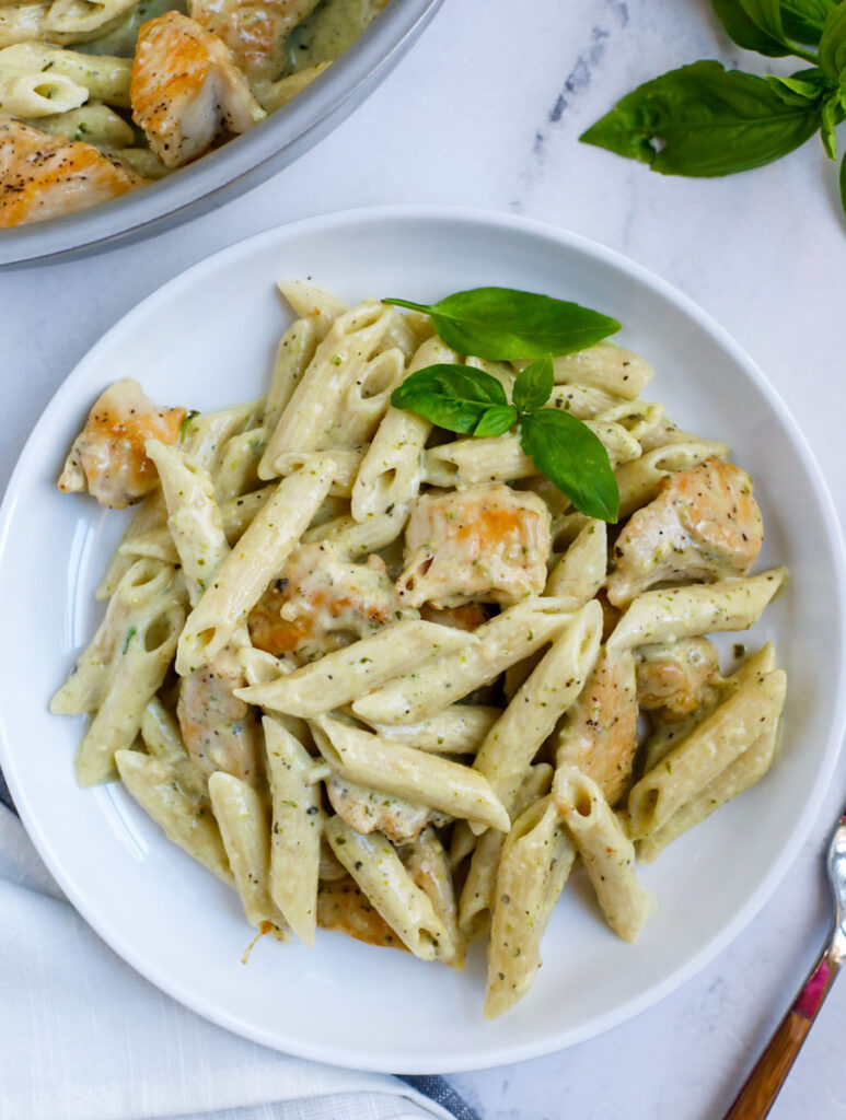A plate of pesto chicken pasta topped with fresh basil.