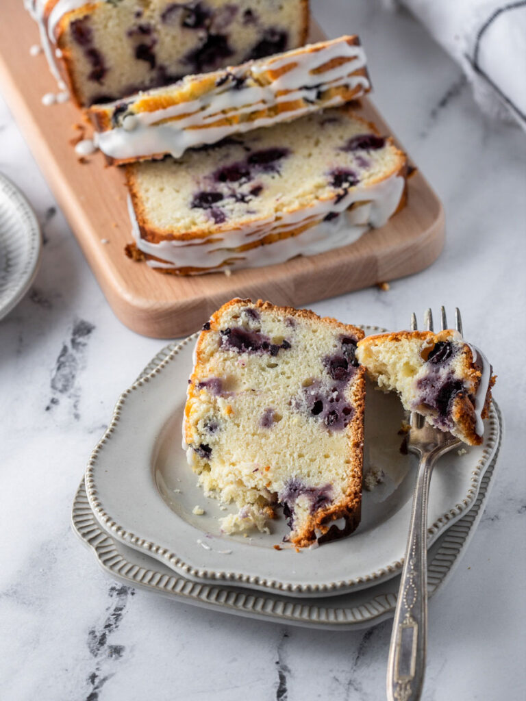 a slice of blueberry lemon bread on a plate with a bite cut off with a fork