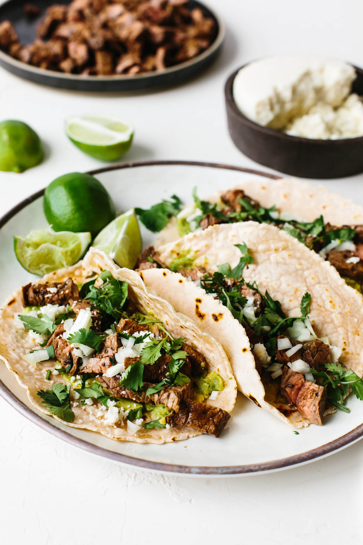 A plate with carne asada tacos next to limes.