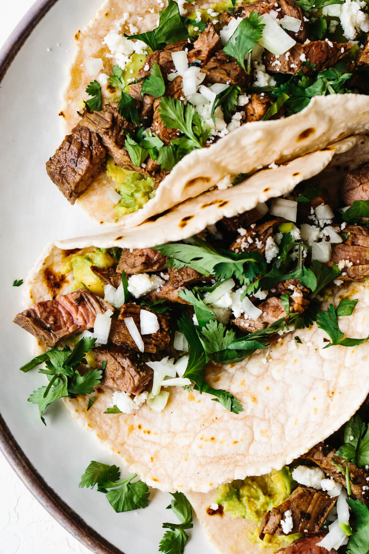 Carne asada tacos next to each other on a plate.