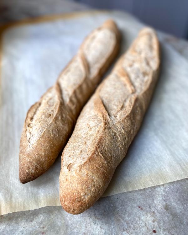 Two whole-wheat baguettes on a counter. 