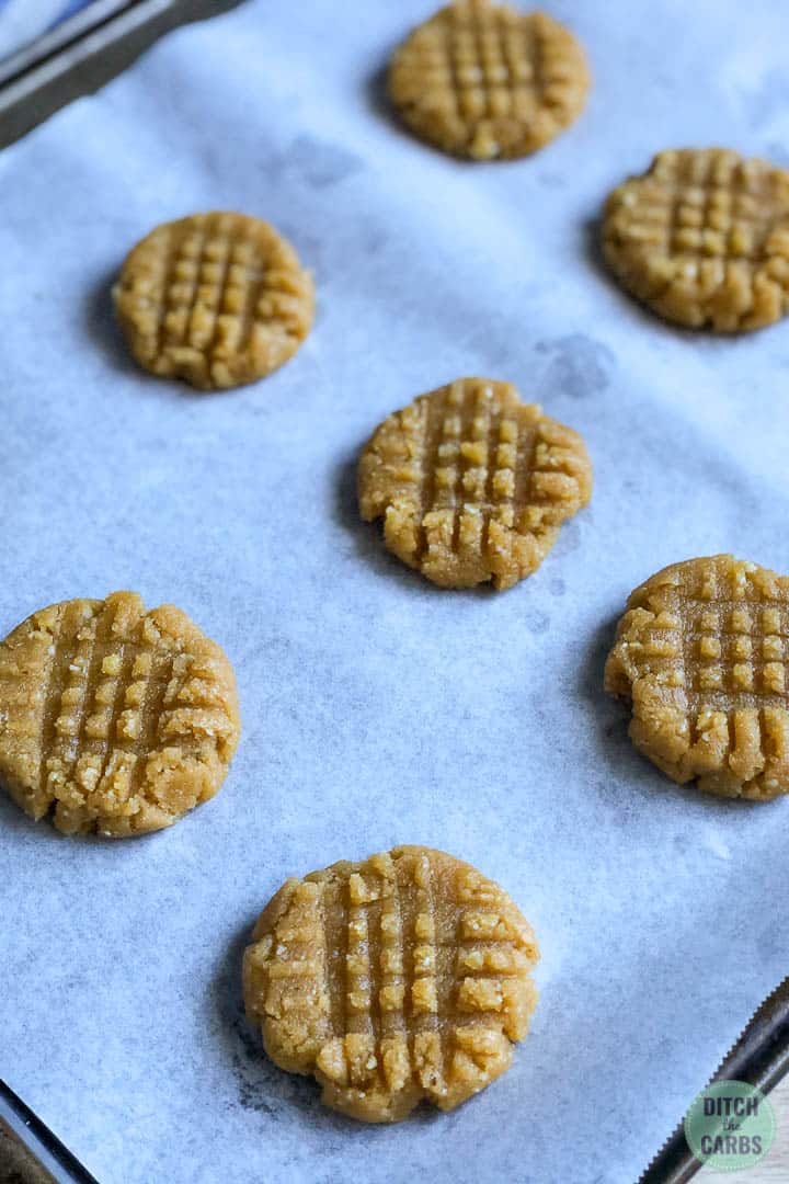 Keto peanut butter cookies arranged on a lined baking sheet ready to be cooked.