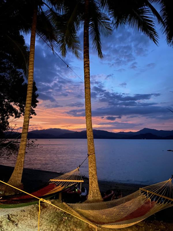 Two hammocks between trees overlooking the ocean and mountains at night. 