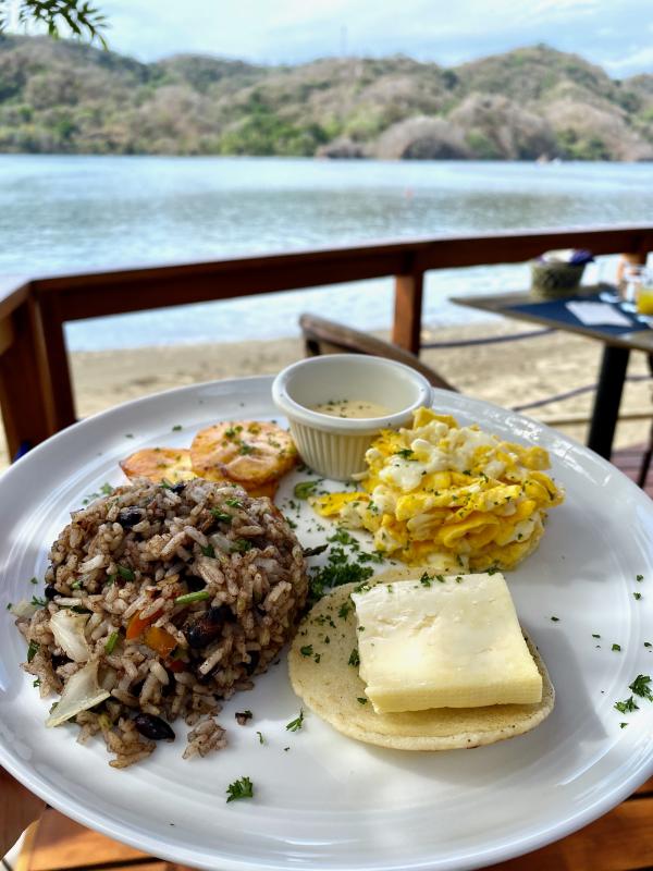 Beans & Rice, cheese, tortilla, and eggs on a plate with the ocean in the background. 