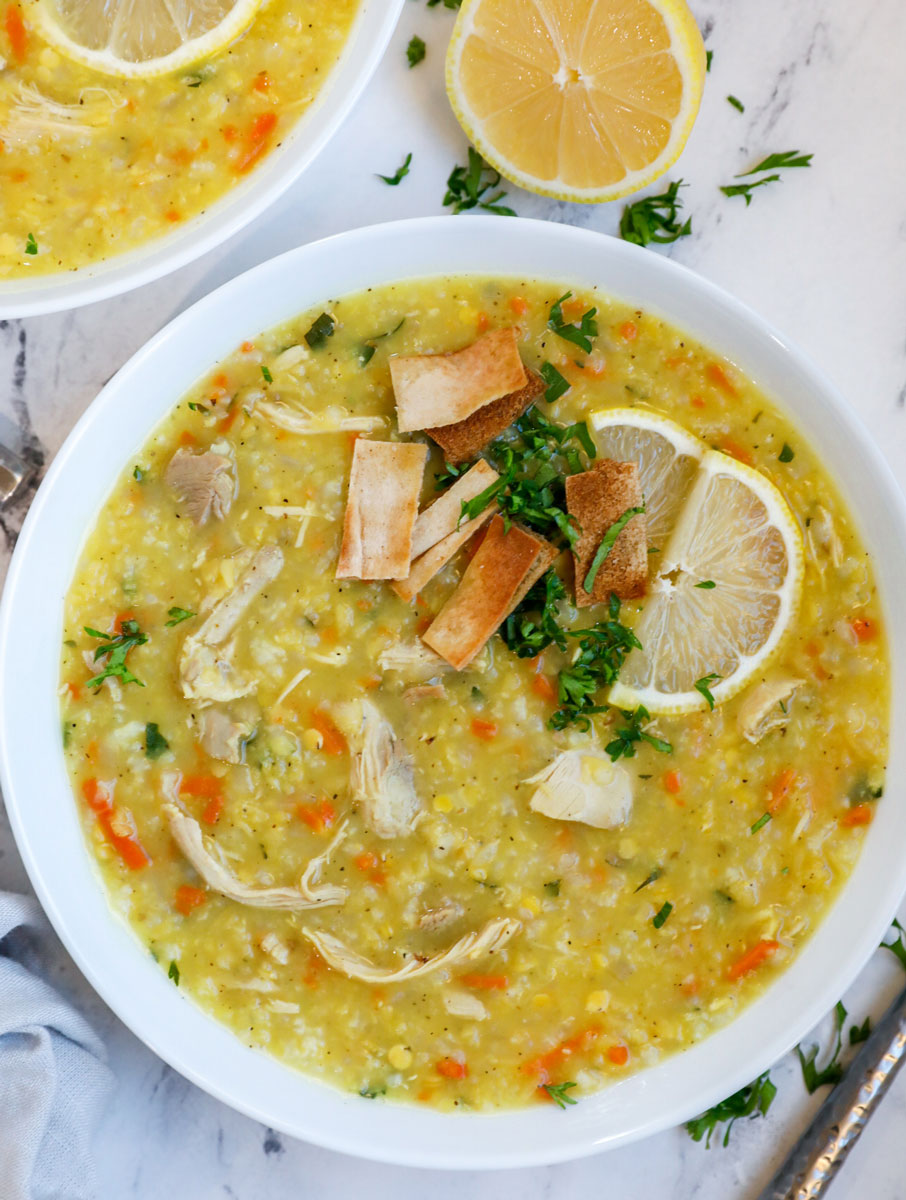 A bowl of chicken lentil and rice soup with sliced lemon and pita chips.