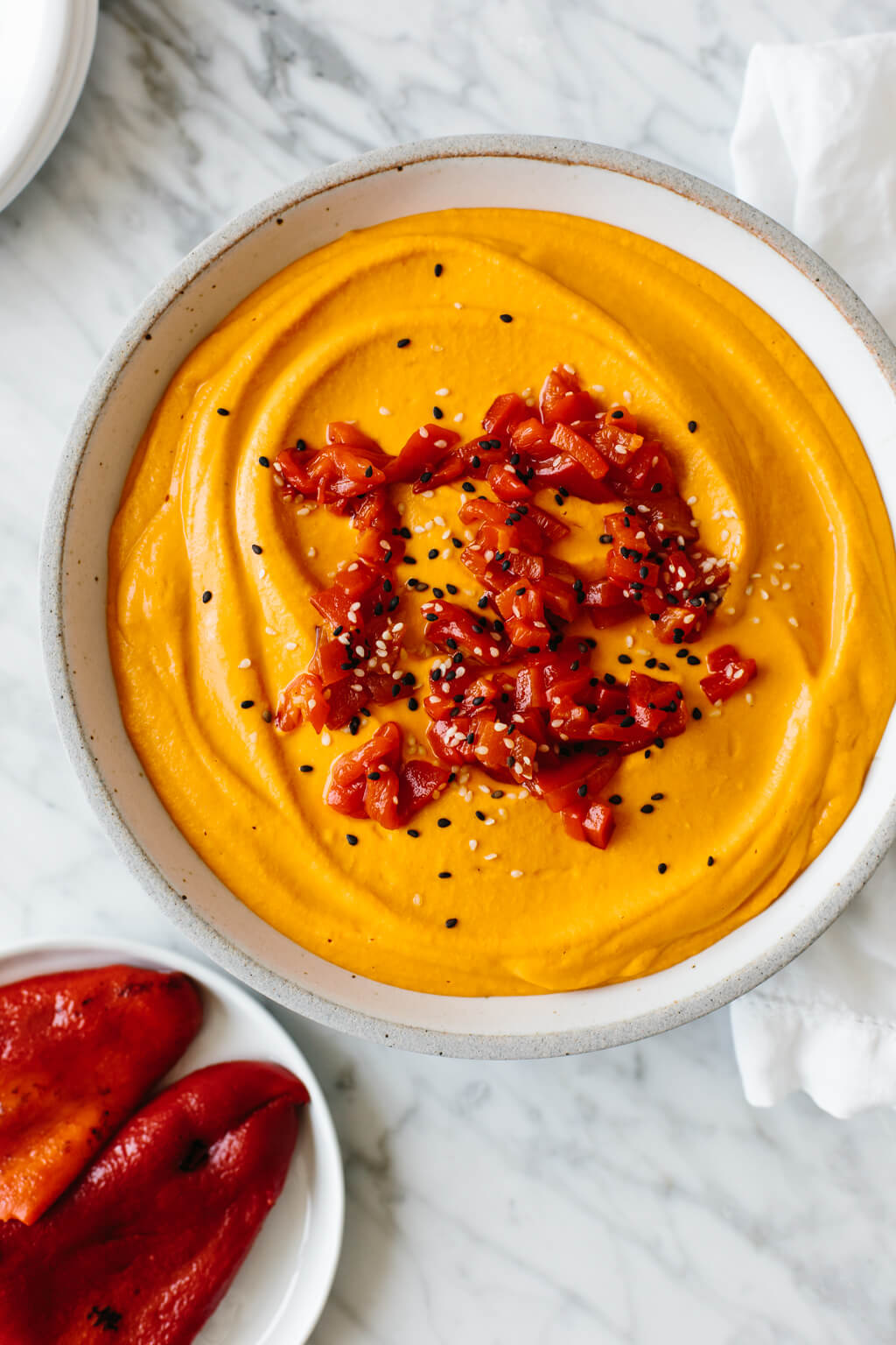 Roasted red pepper hummus in a bowl next to peppers.