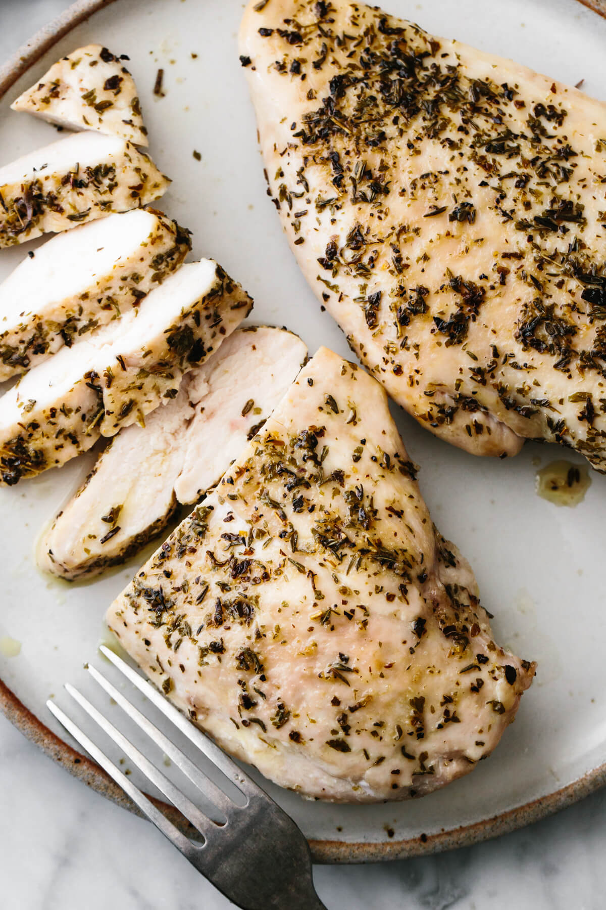 Herb baked chicken breast sliced into pieces on a plate.