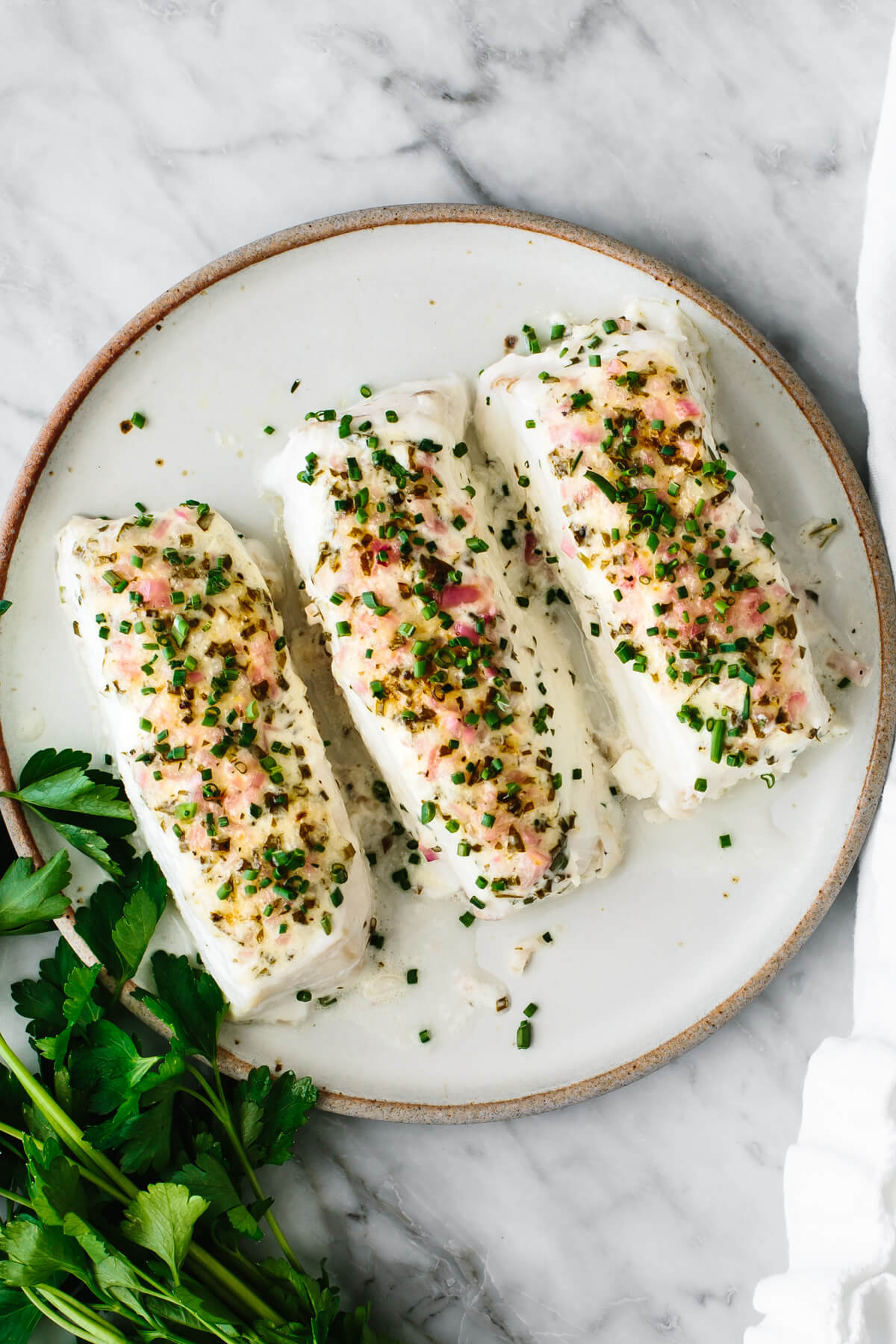 Baked halibut fillets on a plate next to cilantro