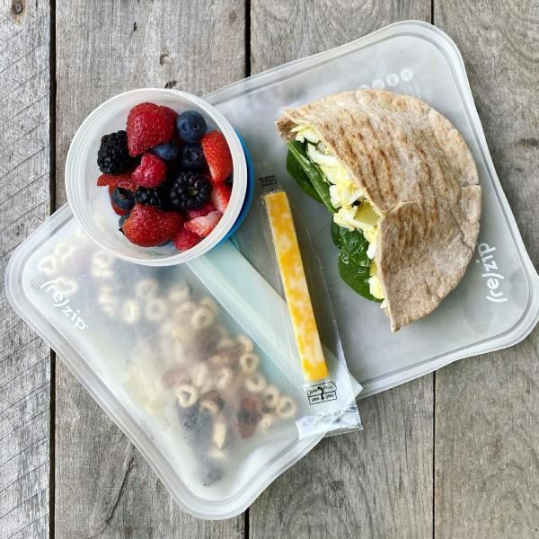Packed school lunch that includes an egg salad sandwich, cheese stick, mixed berries, and homemade trail mix. 