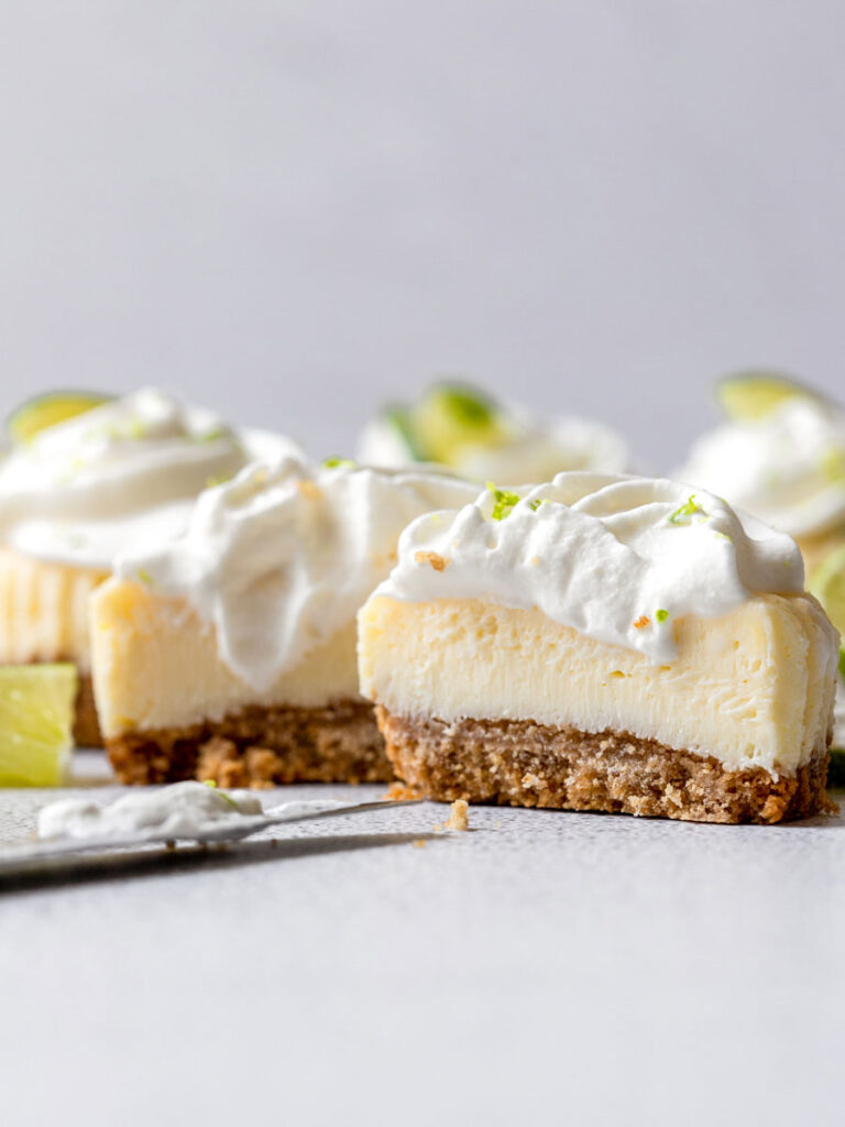 mini keylime cheesecake topped with whipped cream and lime slices and sliced in the middle showing the center