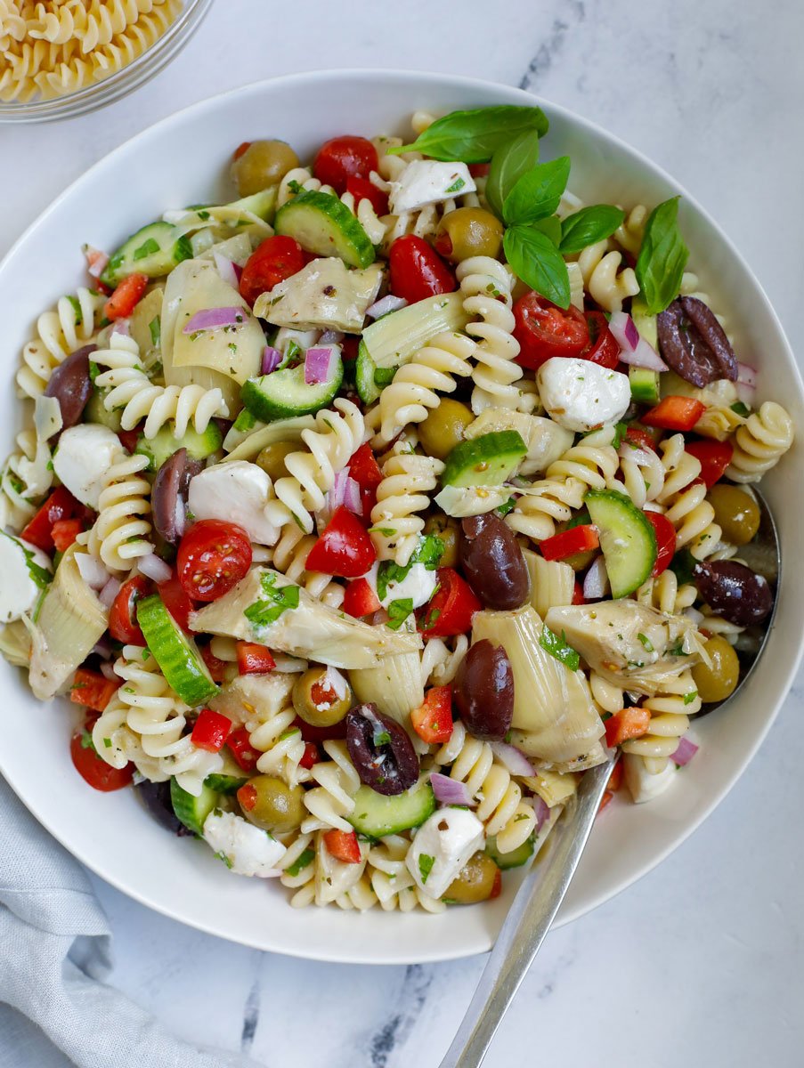 A bowl of Mediterranean pasta salad with a spoon on a marble service.