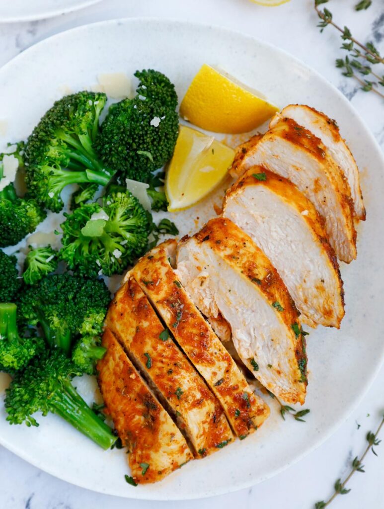 A plate of sliced air fryer rosemary chicken breast beside broccoli.