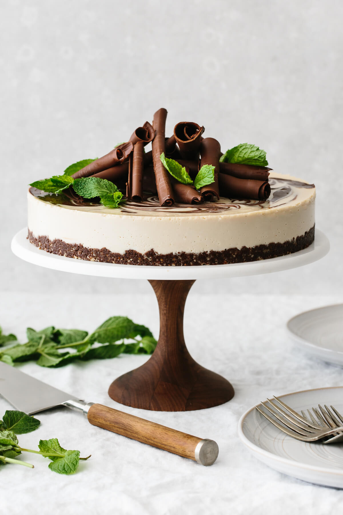 Mint chocolate vegan cheesecake on a cake stand and garnished with chocolate curls and mint leaves.