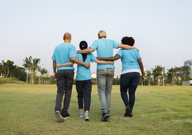 4 people, 2 women, 2 men, wearing light blue t-shirts with their arms round each other. They are stood in a line with their backs to the camera