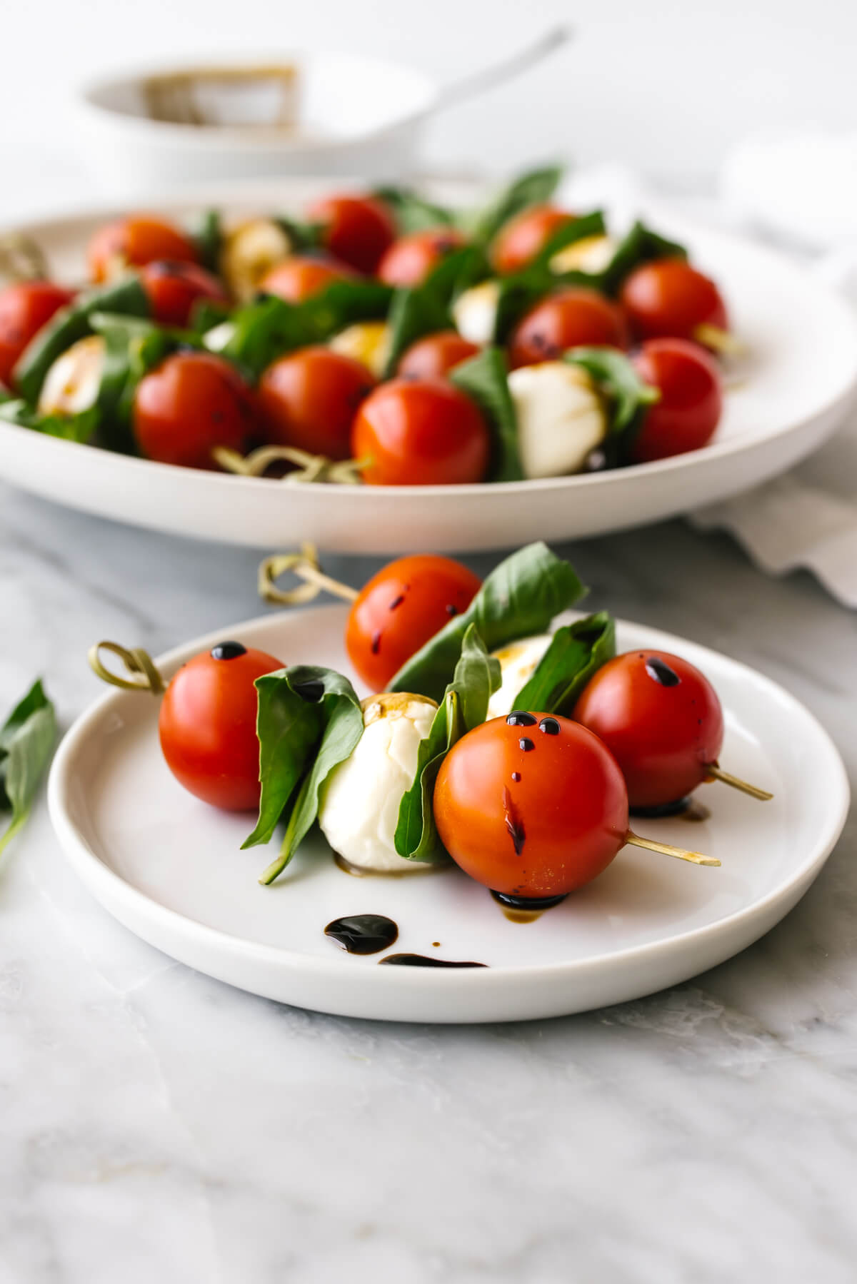 A white plate of caprese skewers next to a napkin.