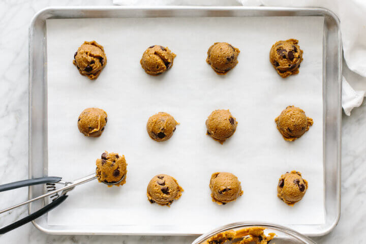 Dolloping cookie dough onto a parchment lined baking sheet.
