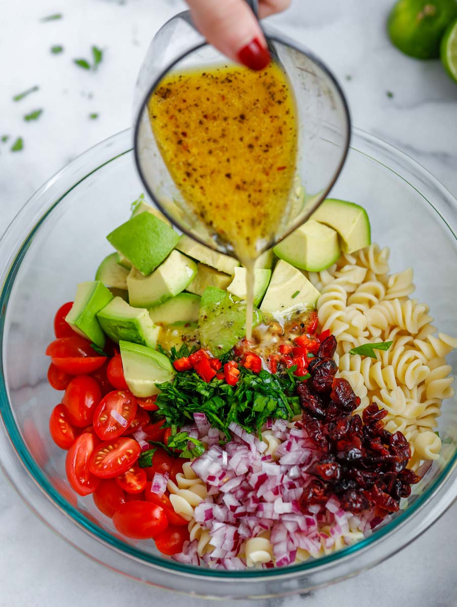 Dressing added to a bowl of avocado chicken pasta salad.