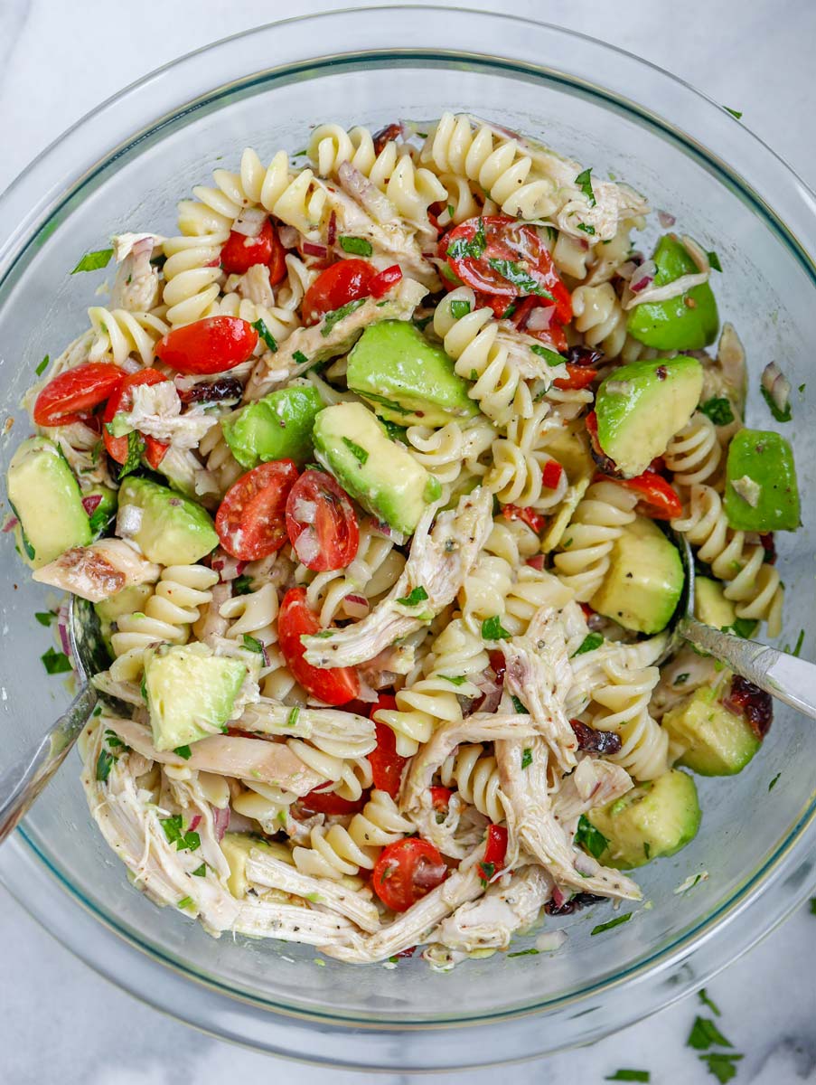 A bowl of avocado chicken pasta salad, mixed with salad dressing.