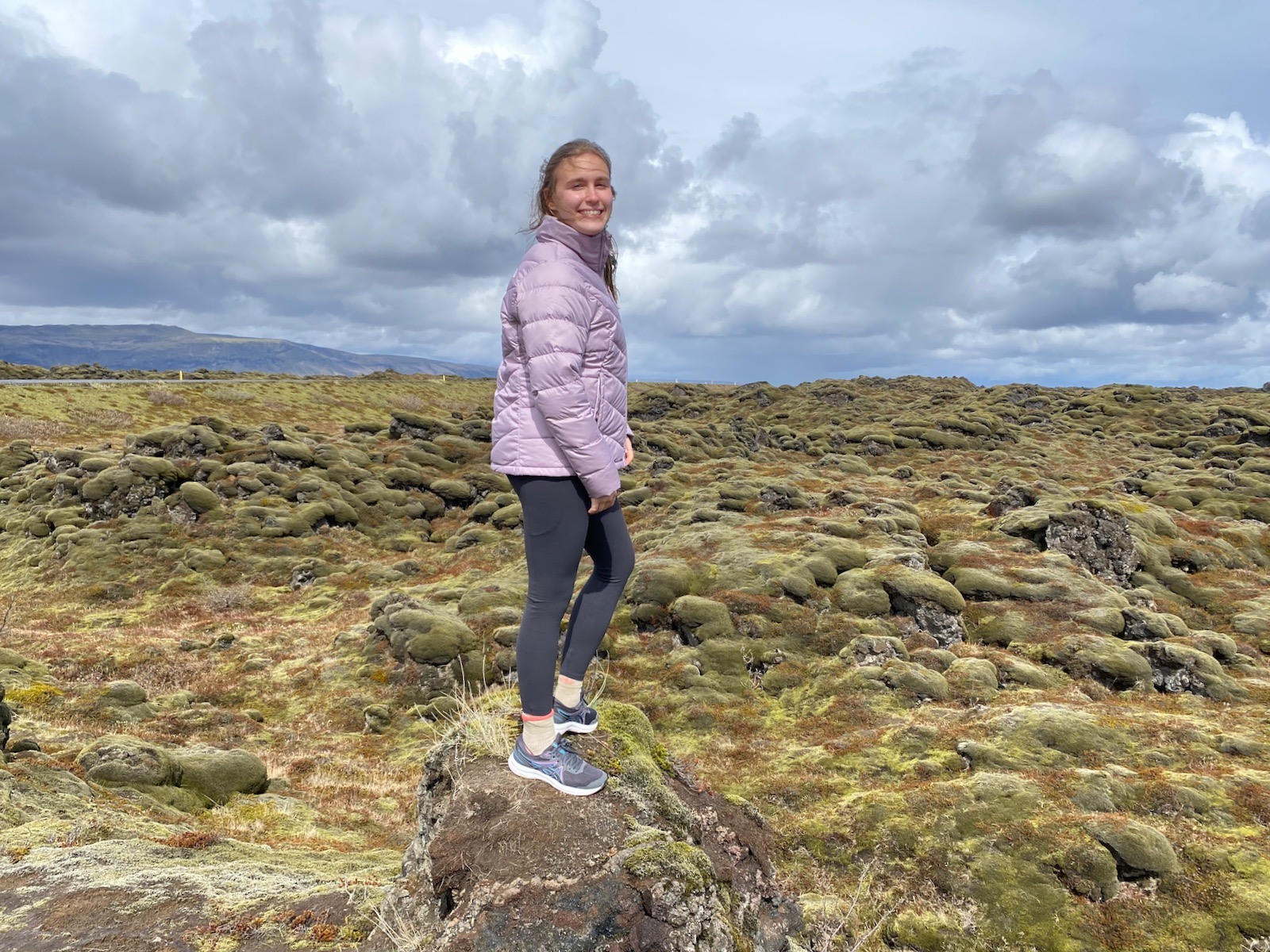 Teen girl standing on moss covered mounds in Iceland. 