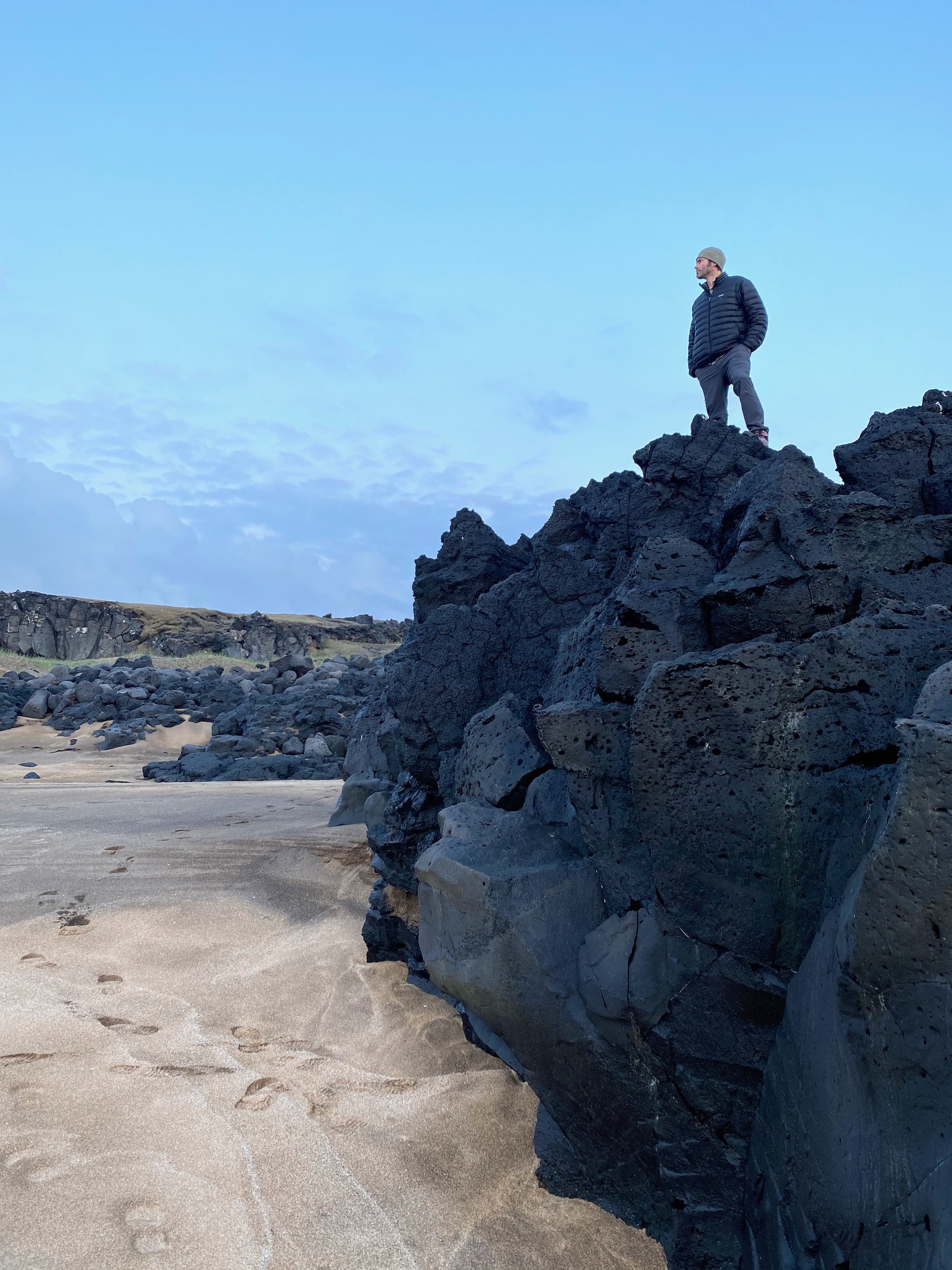 Father posing on top of black rocks at the White Sand beaches in Snæfellsjökull National Park. 