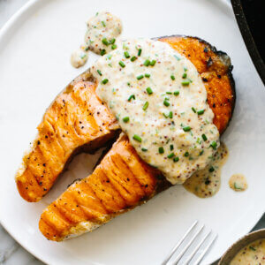 Grilled salmon steak on a plate with garlic chive yogurt sauce