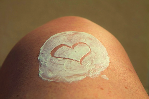 Close up of a woman's knee with a circle of white moisturiser tha has had a hear drawn into it.