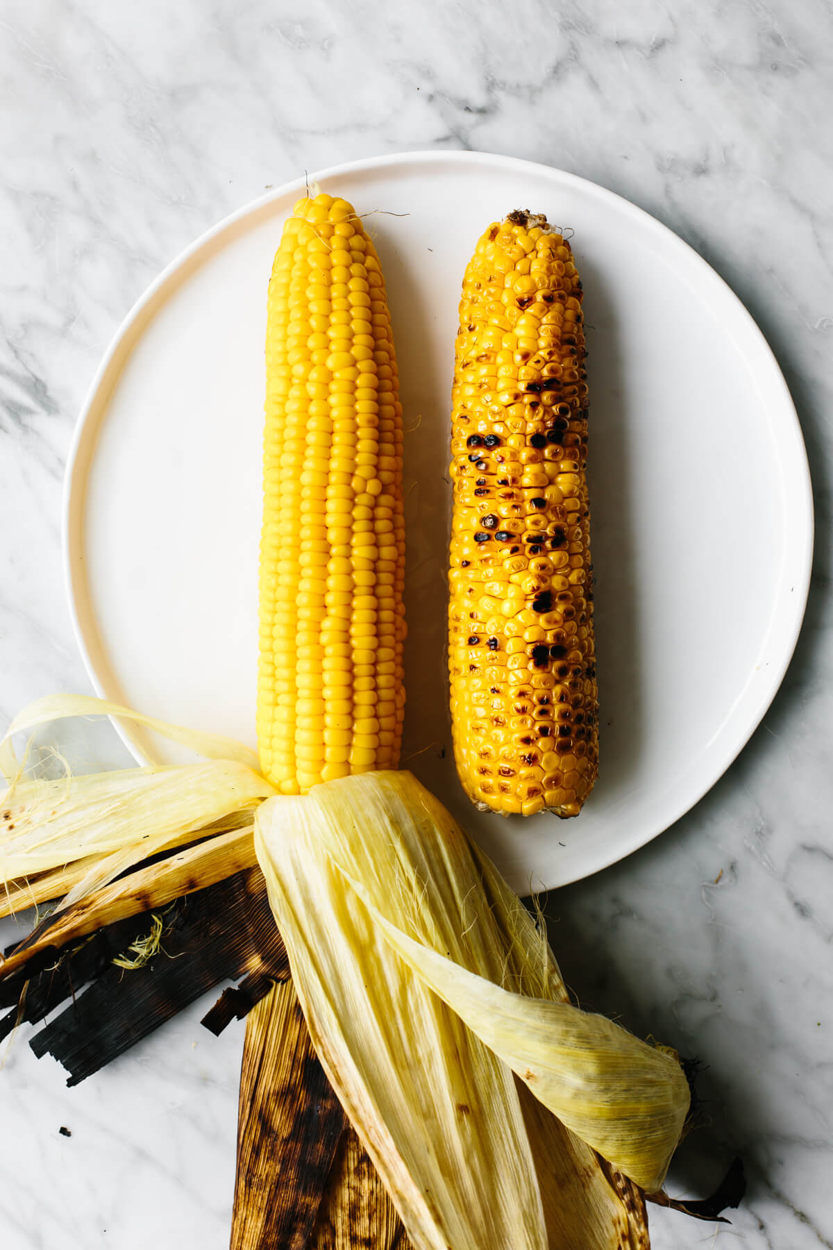 Two grilled corn on the cobs on a white plate