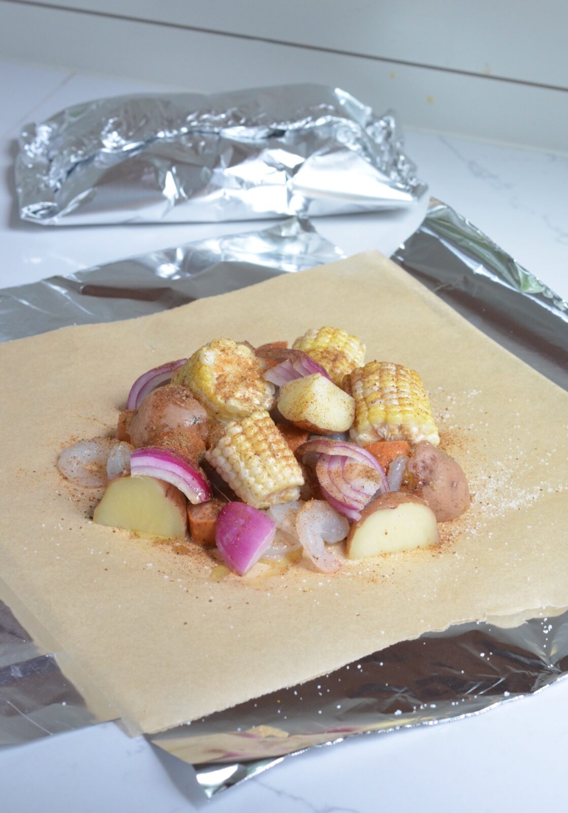 Shrimp, potatoes, corn, onion, and andouille sausage on top of parchment paper and tinfoil. 