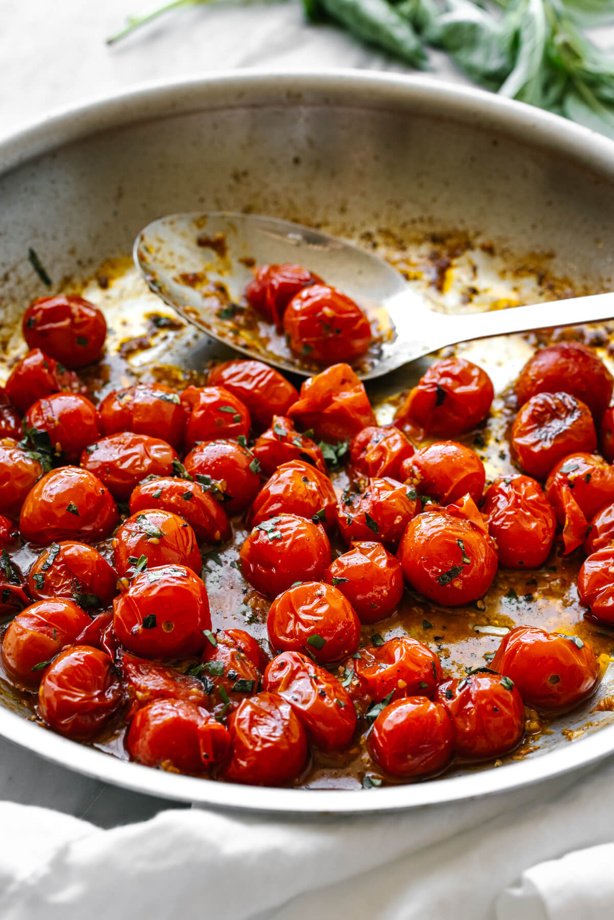 A pan with blistered tomatoes next to basil.