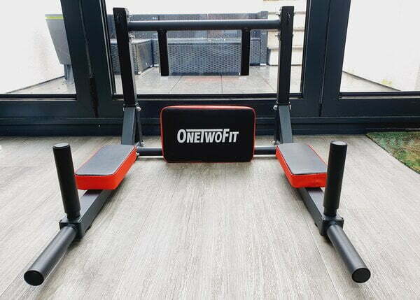 close up picture of the onetwofit wallmounted pull up bar. it is sat on a wooden floor in fron of some glass bi fold doors looking out onto a patio area