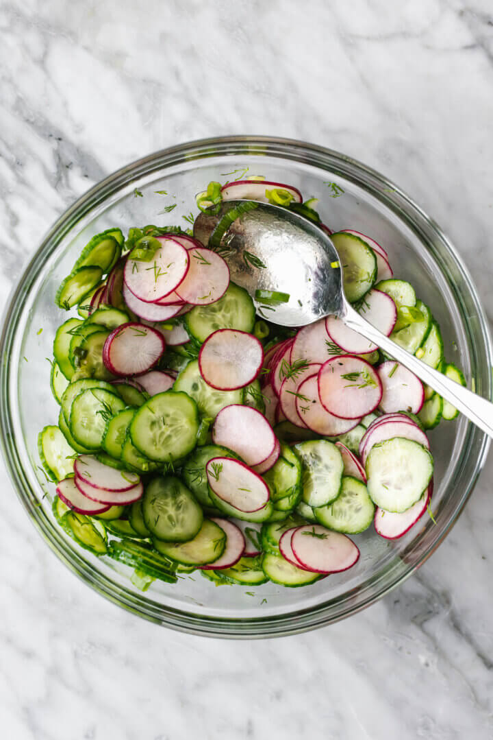 Stirring a cucumber radish salad together in a bowl.