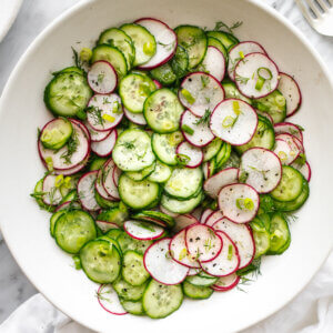 A bowl of cucumber radish salad next to a napkin