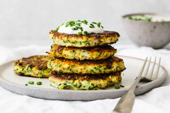 Four zucchini fritters on a plate, topped with sauce and chives.