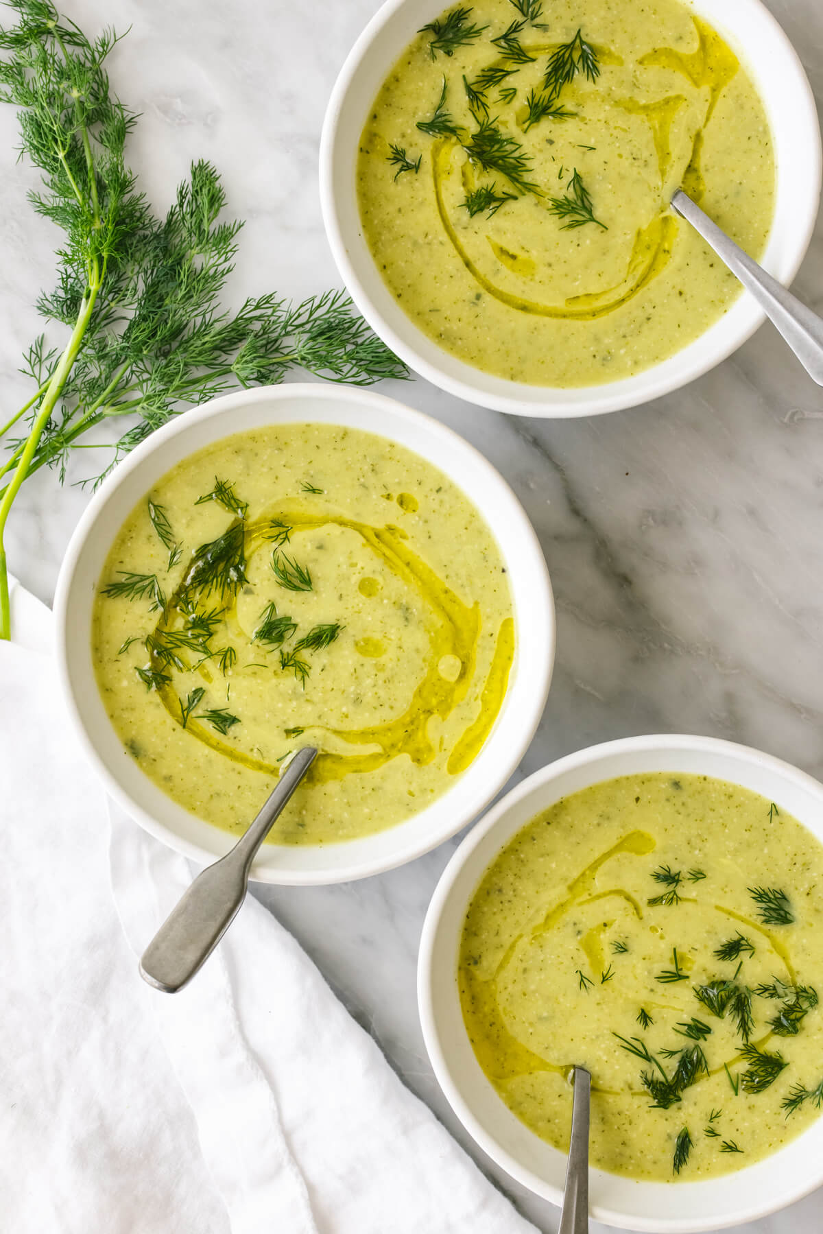 Bowls of zucchini soup next to dill.