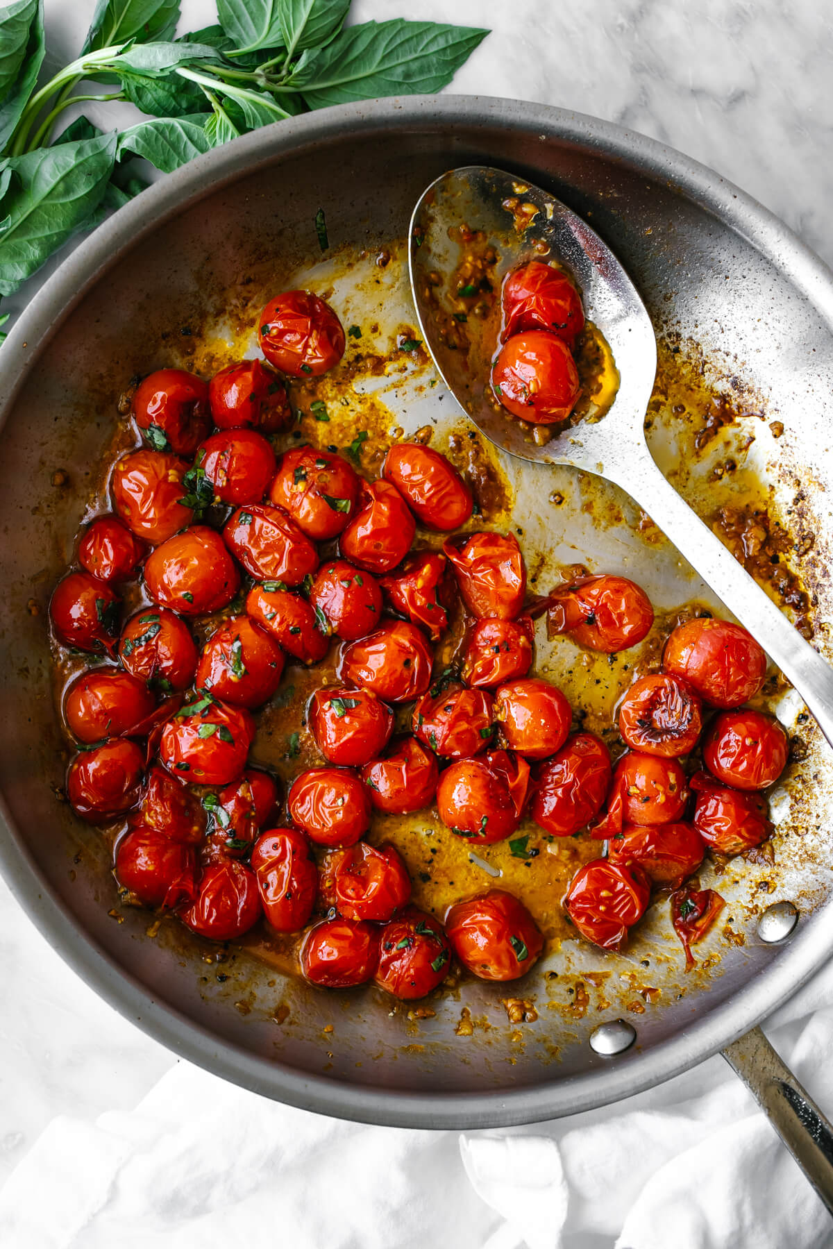 Blistered tomatoes in a pan with a large serving spoon.