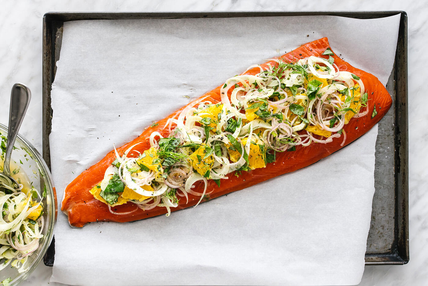 A whole slow roasted salmon with fennel orange topping on a lined baking sheet.