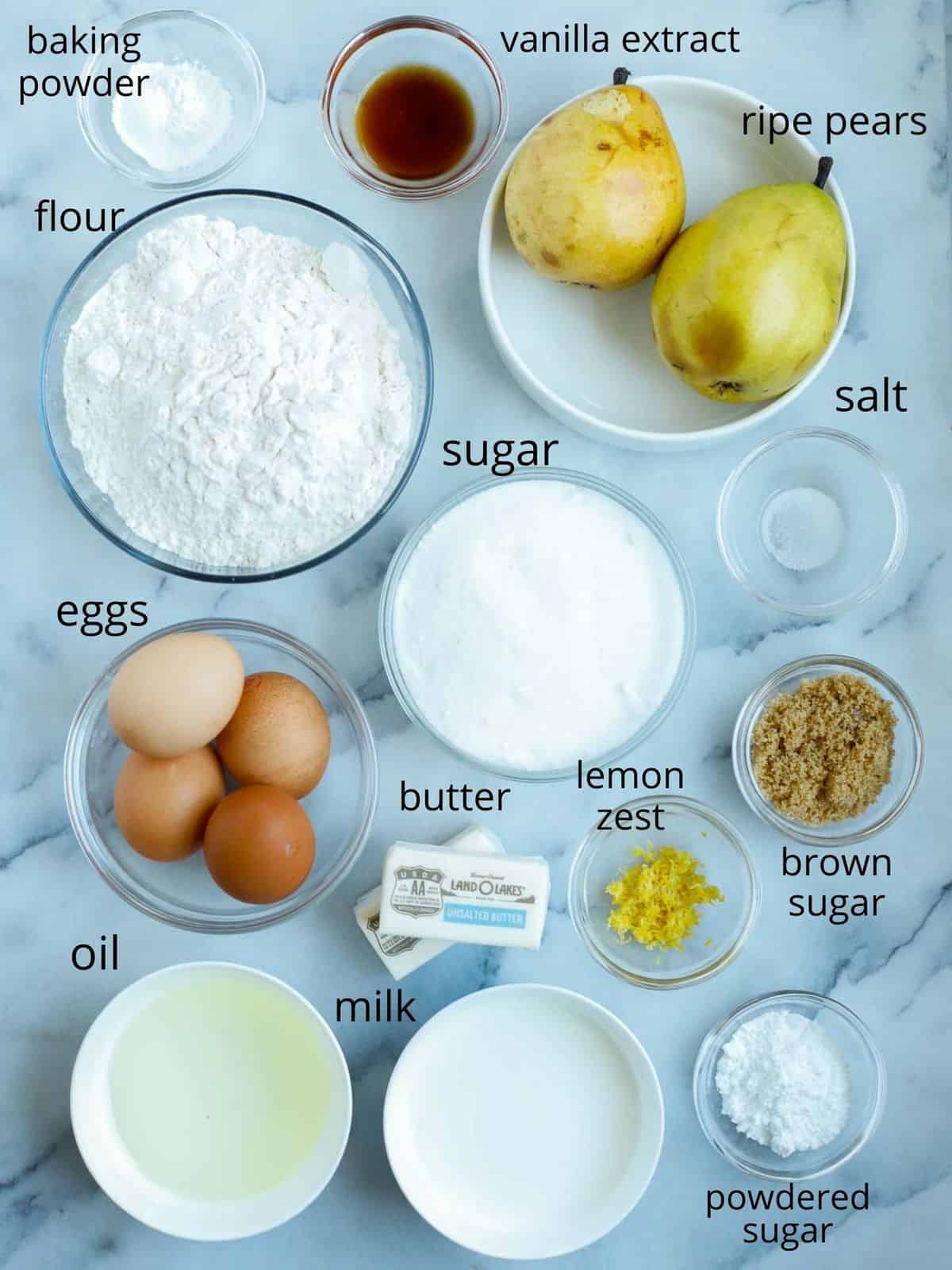 ingredients of the pear cakes in ramekins laid out on a marble slab.