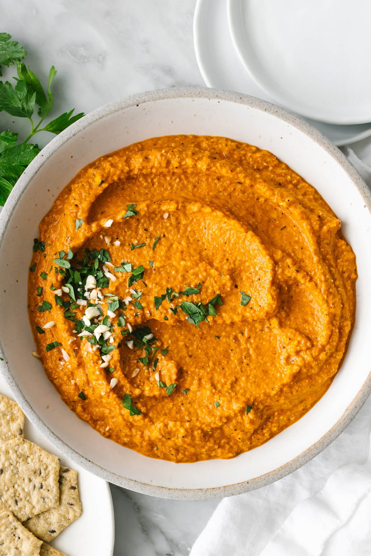 A white bowl of romesco sauce next to a plate of crackers.