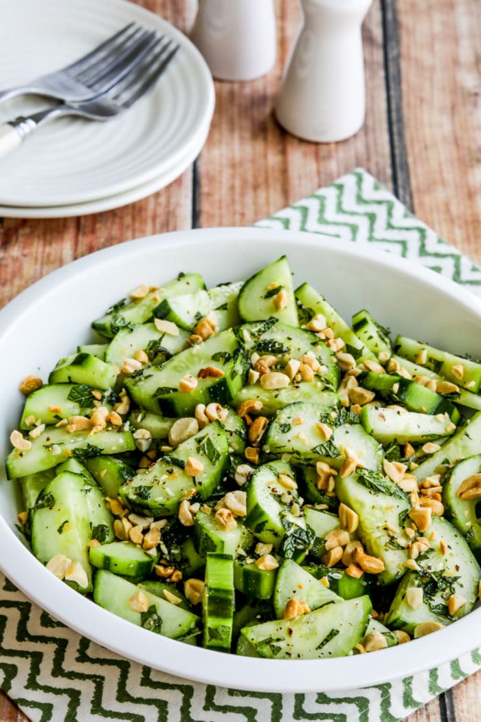 Thai Cucumber Salad in serving bowl with plates, forks, salt, and pepper.