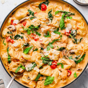creamy-chicken-tortellini-pasta in a skillet, garnished with basil and shaved parmesan cheese