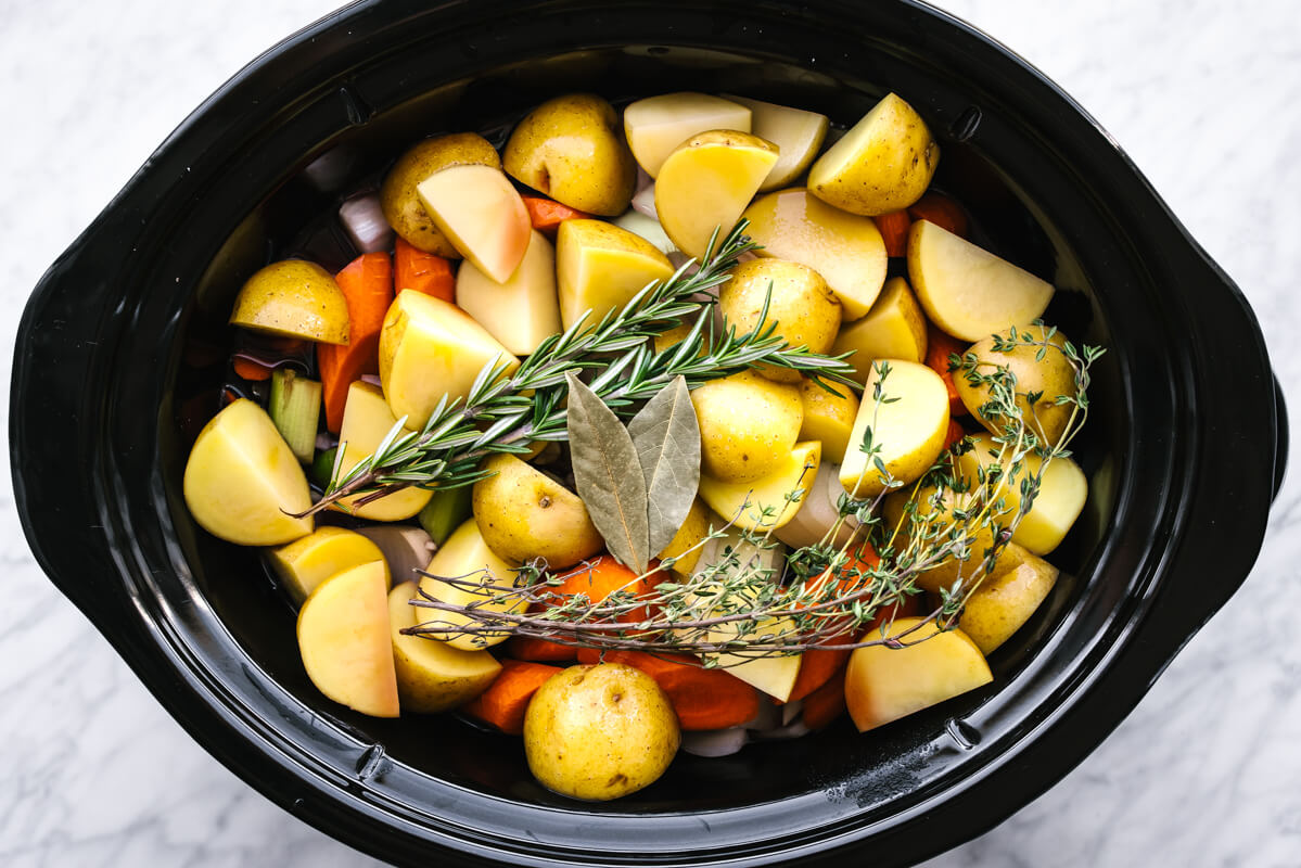 Adding pot roast ingredients into a slow cooker with herbs