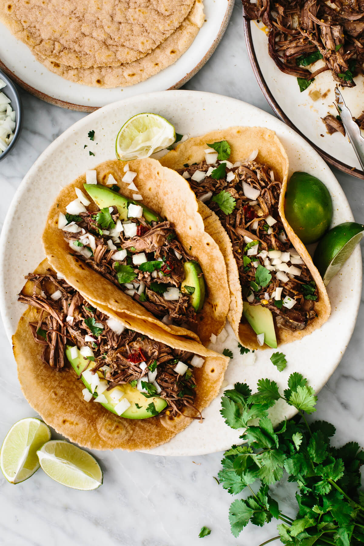 Barbacoa tacos on a plate with cilantro and lime wedges.